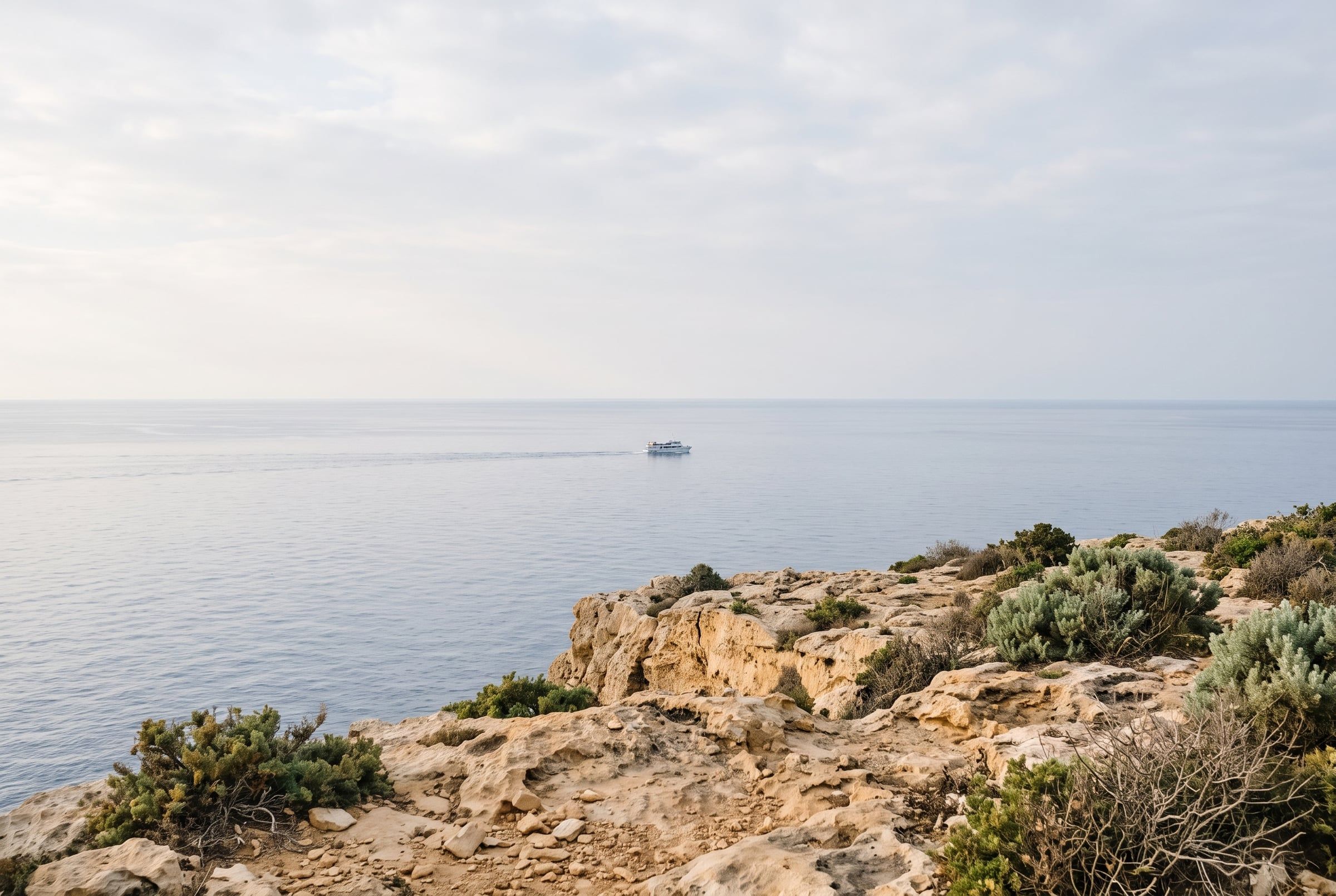 A passenger ferry crossing calm open water, seen from a limestone cliff
